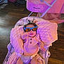 baby, sunglasses, blanket, baby_seat, indoor, wooden_floor, pink, cushion, infant, clothing, person, toddler, headwear, smiling, cute, child, playful, seatbelt, hair, toy
