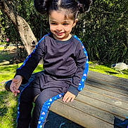 Nyrah is registered to the contest to win money with this photo: child, smiling, outdoor, park, bench, trees, sunlight, black_clothing, blue_stripes, pink_shoes, grass, bird, hair_buns, happy, person, casual_wear, nature, daylight, cute, playful