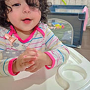 Hazel joined the competition — help win amazing prizes! toddler, child, high_chair, curly_hair, striped_shirt, indoor, playpen, toy, baby, person, happy, smiling, face, table, furniture, curly, cute, infant, clothing, hands