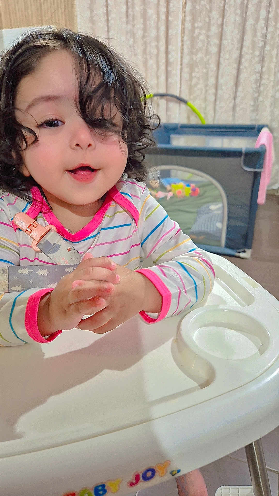 Hazel joined the competition — help win amazing prizes! toddler, child, high_chair, curly_hair, striped_shirt, indoor, playpen, toy, baby, person, happy, smiling, face, table, furniture, curly, cute, infant, clothing, hands