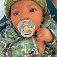 Nathan is registered to the contest to win money with this photo: baby, infant, child, portrait, close_up, pacifier, beanie, hat, plaid, clothing, green, sitting, hand, eyes, face, indoors, cozy, blanket, photography, adorable