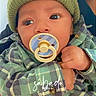 baby, infant, child, portrait, close_up, pacifier, beanie, hat, plaid, clothing, green, sitting, hand, eyes, face, indoors, cozy, blanket, photography, adorable