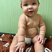 Braiden joined the competition — help win amazing prizes! baby, infant, child, diaper, bare_skin, sitting, blanket, brown_blanket, hand, foot, face, curly_hair, cute, chubby, expression, indoors, green_wall, soft_light, portrait, candid