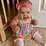 Hailey is registered to the contest to win money with this photo: baby, child, smiling, headband, bow, colorful_clothing, striped_dress, carpet, sitting, wooden_chair, wooden_sign, seven_months, cute, happy, indoors, toddler, sock, pink, playful, portrait