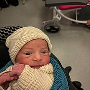 Maïlhow participe au concours pour gagner de l'argent avec cette photo : newborn, baby, knit_hat, knit_sweater, blue_blanket, infant, wrapped, indoor, hospital, medical_equipment, red_chair, person, cute, face, young_child, holding, portrait, warm, soft, human