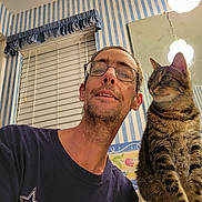 Nicki joined the competition — help win amazing prizes! man, glasses, beard, cat, tabby_cat, indoor, bathroom, mirror, light_fixture, window, blinds, wallpaper, striped_wallpaper, counter, smile, facial_hair, pet, curious, portrait, selfie