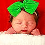newborn, baby, infant, sleeping, green_bow, headband, blanket, white_blanket, red_background, face, peaceful, cute, wrapped, portrait, closeup, soft_texture, skin, tiny_hands, resting, indoors