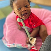 Axxel joined the competition — help win amazing prizes! baby, child, smiling, happy, portrait, red_outfit, pink_seat, toy, teething_toy, indoor, sitting, infant, dark_skin, curly_hair, face, eyes, open_mouth, colorful_background, close_up, family_photo