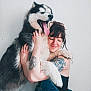 affection, casual_clothing, closeup, companion, dog, friendship, fur, happy, hug, husky, indoor, long_hair, pet, portrait, smile, tattoo, tongue, white_background, woman, yawn
