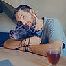 Billy a rejoint le concours — aidez-le/la à gagner de superbes lots ! man, dog, pet, human, face, beard, hugging, affection, portrait, indoors, table, drink, glass, blue_shirt, bracelet, necklace, seated, home, love, text_overlay