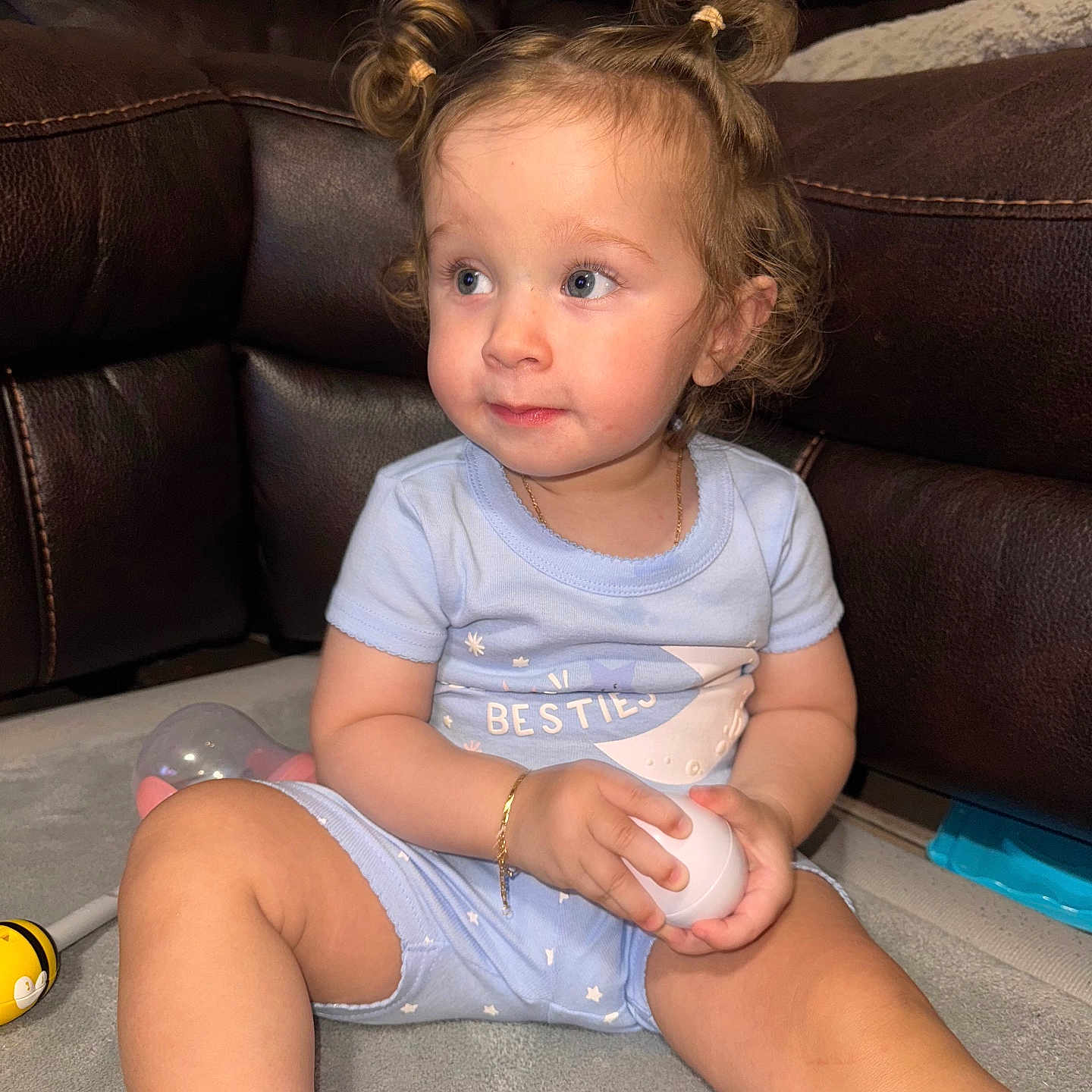 Aurora is registered to the contest to win money with this photo: baby, blue_clothing, bracelet, carpet, casual, child, comfortable, curly_hair, cute, floor, indoor, leather_couch, looking_away, person, pigtails, playful, sitting, soft_lighting, toddler, toy