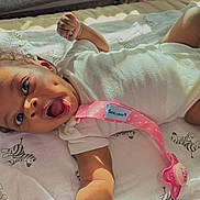 Kaylee joined the competition — help win amazing prizes! baby, infant, smiling, pacifier, blanket, zebra_pattern, onesie, curly_hair, dimples, sunlight, shadow, hand, face, mouth_open, lying_down, cute, child, indoor, fabric, pink