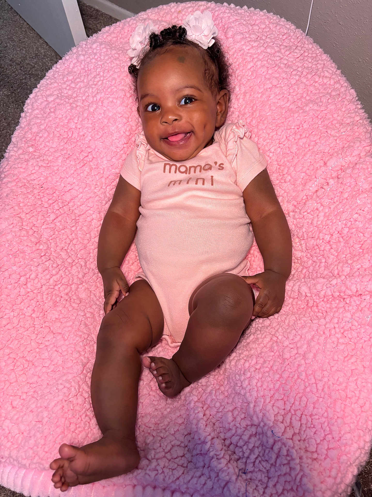 Kaylee is registered to the contest to win money with this photo: baby, infant, smiling, pink_blanket, onesie, flower_headband, dimples, cute, happy, indoor, child, person, skin, foot, hand, face, hair, lying_down, soft_texture, carpet