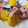 baby, bed, blanket, child, closeup, cute, eyes, face, hand, happy, infant, laughing, onesie, open_mouth, plush_toy, portrait, smiling, soft_texture, toy, yellow_clothing