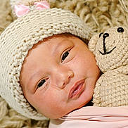 Anila joined the competition — help win amazing prizes! baby, infant, knitted_hat, pink_bow, crocheted_toy, teddy_bear, blanket, soft_texture, sleepy, closeup, cute, child, face, newborn, cozy, warm, wrapped, portrait, indoor, comfort