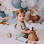 toddler, child, toy, wooden_toy, stacking_toy, teddy_bear, balloons, crescent_moon, clouds, airplane_toy, indoor, portrait, cute, playful, soft_lighting, nursery, smiling, sitting, baby_clothes, decor