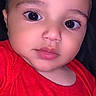 Ali joined the competition — help win amazing prizes! baby, infant, child, portrait, close_up, face, wide_eyes, looking_at_camera, red_shirt, clothing, indoors, dark_background, phone_screenshot, photograph, head, eyes, nose, mouth, cute, sitting