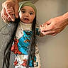baby, child, infant, portrait, indoors, pajamas, cookie_monster, green_hat, long_hair, wide_eyes, looking_at_camera, adult_hands, playful, colorful_clothing, cartoon_characters, gray_wall, standing, family, close_up, funny_pose
