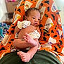 baby, infant, blanket, orange, mittens, lying_down, cute, indoors, soft_texture, pattern, foot, hand, skin, face, newborn, relaxed, colorful, person, comfort, cozy