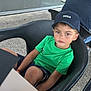 child, boy, green_shirt, cap, hat, black_chair, outdoor, table, fork, knife, person, casual, seated, shorts, face, looking, calm, daylight, restaurant, patio
