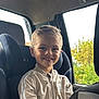 child, boy, smiling, car_seat, beige_jacket, adidas, window, car_interior, seat, happy, young, portrait, casual_clothing, light, daylight, outdoor_view, greenery, hair, face, person