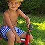 child, boy, smile, hat, straw_hat, tricycle, outdoor, grass, greenery, summer, shorts, striped_shorts, sunlight, play, toy, happy, portrait, bare_chest, nature, casual