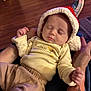 baby, sleeping, hat, red, white, cream, clothing, person, arms, tattoo, floor, wooden_floor, indoor, cozy, infant, cute, relaxed, portrait, peaceful, child