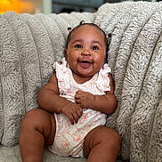 Kaylee joined the competition — help win amazing prizes! baby, smiling, happy, infant, sitting, couch, plush, textured, hair_ties, cute, indoors, cozy, child, person, skin, clothing, room, furniture, portrait, relaxed