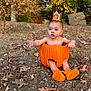 baby, pumpkin, autumn, fall_leaves, outdoor, crown, orange_booties, baby_in_pumpkin, nature, child, seasonal, cute, sitting, grass, trees, leaf_litter, expression, holiday, costume, young_child