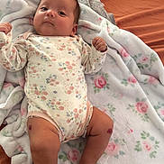 Ivy is registered to the contest to win money with this photo: baby, child, infant, portrait, lying_down, blanket, floral_blanket, bed, bedroom, onesie, floral_clothing, face, hands, legs, feet, looking_at_camera, indoors, cozy, cute, photography
