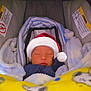 baby, sleeping, car_seat, blanket, santa_hat, child, infant, cozy, warm, soft_texture, yellow_blanket, blue_blanket, striped_fabric, cute, holiday, festive, face, peaceful, indoors, wrapped_up