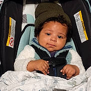 Josiah is registered to the contest to win money with this photo: baby, child, infant, car_seat, knitted_hat, blanket, winter_clothing, jacket, fleece, harness, safety_buckle, portrait, indoor, sitting, calm, face, eyes, hands, textile, photography