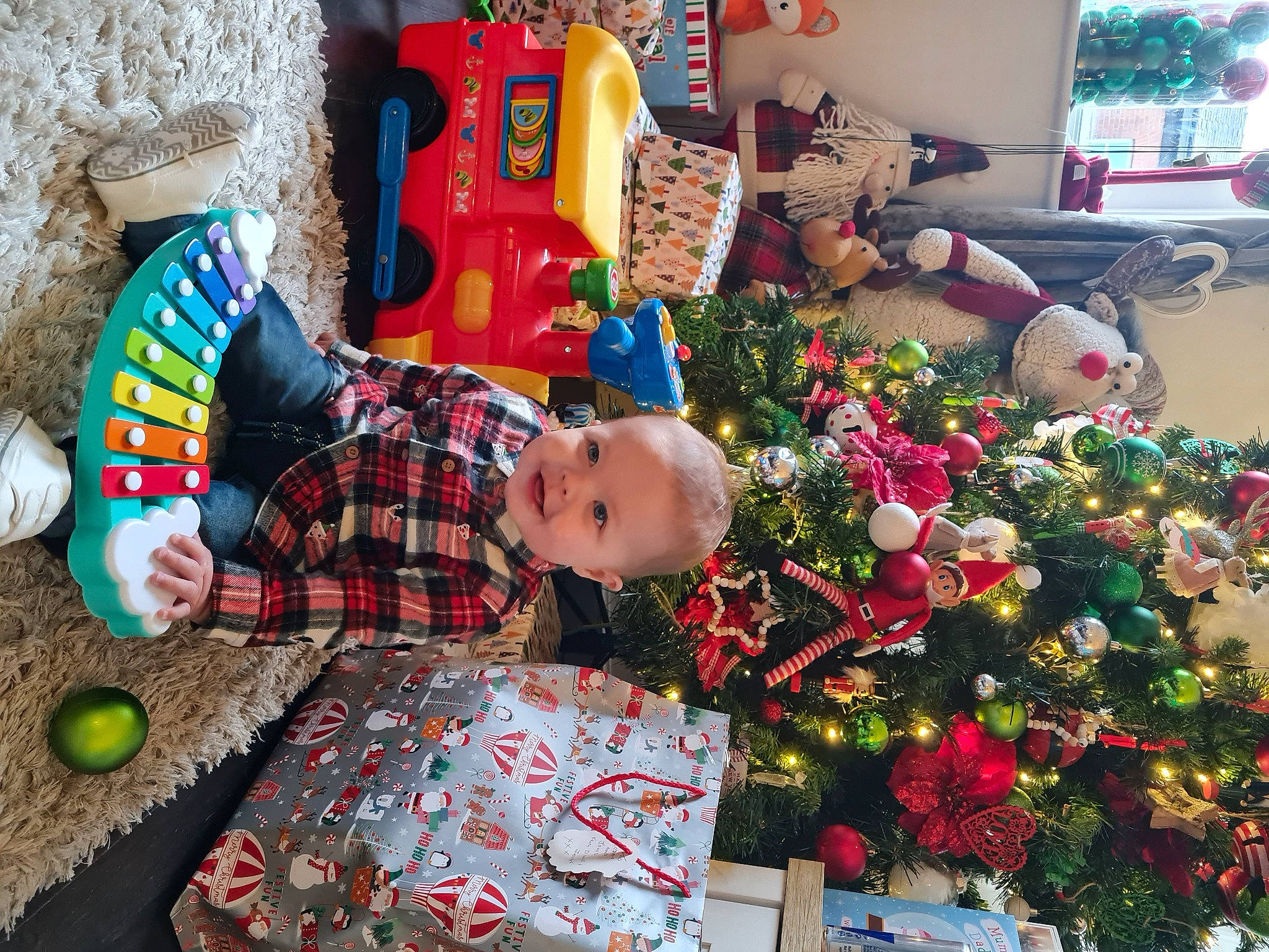 Ellis is registered to the contest to win money with this photo: baby, baby_toddler_clothing, child, christmas, christmas_tree, event, fun, green, holiday, home, joy, lap, pattern, person, plaid, plant, red, room, stuffed_toy, toddler