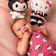Kiara is registered to the contest to win money with this photo: baby, infant, smiling, hello_kitty, plush_toys, pink_clothing, cute, soft_blanket, cheerful, indoor, portrait, child, toy, cuddly, happy, playful, lying_down, fingers_in_mouth, doll, colorful