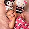 baby, infant, smiling, hello_kitty, plush_toys, pink_clothing, cute, soft_blanket, cheerful, indoor, portrait, child, toy, cuddly, happy, playful, lying_down, fingers_in_mouth, doll, colorful