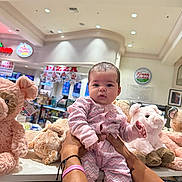Kiara joined the competition — help win amazing prizes! baby, child, person, stuffed_animal, plush_toy, pink_clothing, indoor, store, shopping, display, holding, hands, face, head, soft_toy, cute, pajamas, shelf, retail, bright_lighting