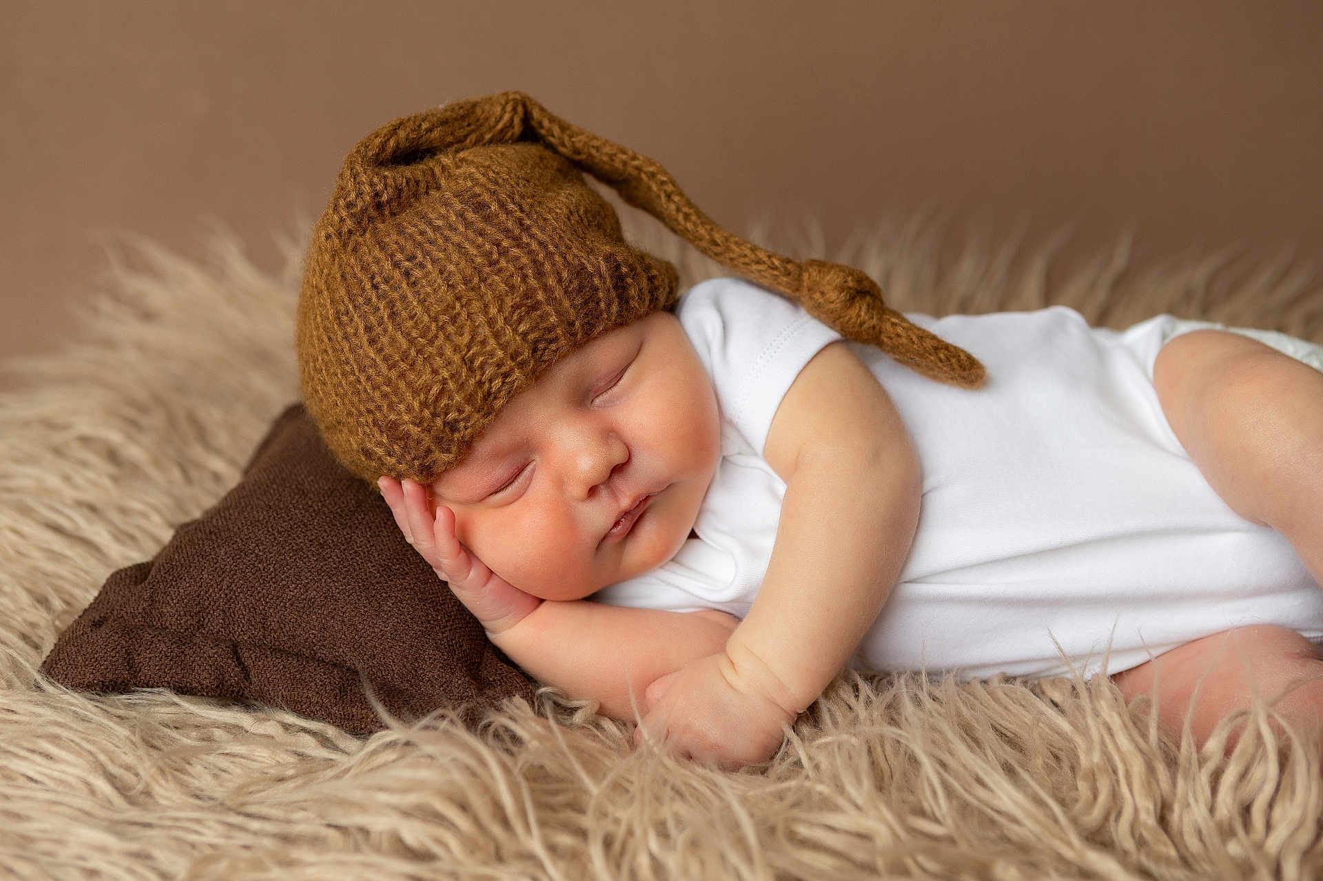 Jordan joined the competition — help win amazing prizes! baby, newborn, sleeping, hat, knitted_hat, pillow, white_onesie, fluffy_rug, brown, cozy, infant, resting, peaceful, cute, soft_texture, portrait, child, indoors, closeup, sleep