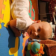 Vojta participe au concours pour gagner de l'argent avec cette photo : baby, child, toy, plush_toy, colorful, foam_mat, floor, indoor, white_clothing, curious, infant, crawling, head, face, play, soft_toy, person, home, puzzle_mat, cute