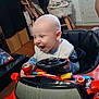 baby, bald, bib, bookshelf, child, floor, furniture, happy, indoor, joyful, person, play, red, room, seat, smiling, steering_wheel, table, toy, toy_car