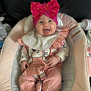 Lyna participe au concours pour gagner de l'argent avec cette photo : baby, infant, pink_bow, baby_seat, tongue_out, smiling, cute, clothing, bib, pink_overalls, cat_design, socks, indoor, happy, child, face, person, comfort, seat, cushion