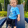 Nicklas is registered to the contest to win money with this photo: toddler, child, outdoor, blue_shirt, black_shorts, sneakers, chair, fence, greenery, curly_hair, determined_expression, sidewalk, grass, daylight, casual_clothing, person, young_child, summer, playful, park