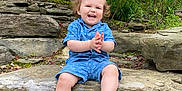 Nicklas is registered to the contest to win money with this photo: toddler, child, smiling, clapping, blue_clothing, shorts, outdoor, rocks, flowers, greenery, nature, garden, happy, sitting, shoes, plants, sunlight, daytime, cute, portrait