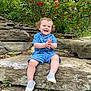 toddler, child, smiling, clapping, blue_clothing, shorts, outdoor, rocks, flowers, greenery, nature, garden, happy, sitting, shoes, plants, sunlight, daytime, cute, portrait