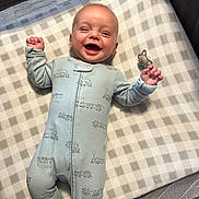 Luca is registered to the contest to win money with this photo: baby, smiling, infant, onesie, sleepwear, crib, pacifier, checkered_pattern, happy, lying_down, face, hand, footed_pajamas, fabric, mesh, toy, cute, child, indoor, sleeping_area