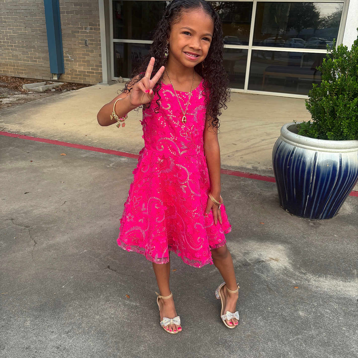 Akijah joined the competition — help win amazing prizes! accessories, bracelet, building, child, curly_hair, earrings, fashion, girl, greenery, happy, high_heels, necklace, outdoor, pavement, peace_sign, pink_dress, planter, pose, smile, window