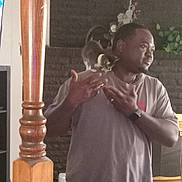 Lola is registered to the contest to win money with this photo: man, human, kitten, cat, pet, shoulder, indoor, living_room, fireplace, brick_wall, plant, wood_pole, t_shirt, watch, ring, standing, looking_right, hand_gesture, television, casual