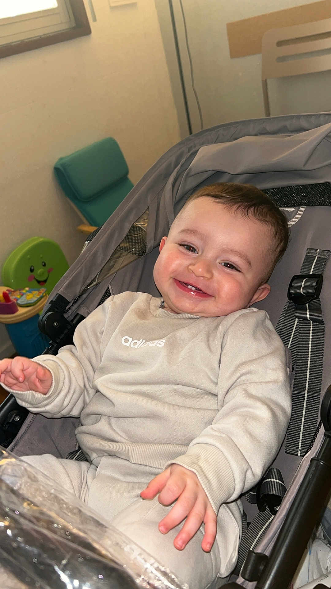 Tariq a rejoint le concours — aidez-le/la à gagner de superbes lots ! baby, infant, stroller, smile, teeth, chubby_cheeks, hand, sweatshirt, adidas_logo, beige_outfit, seat_harness, buckle, toy, playroom, chair, window, indoor, portrait, happy, hair