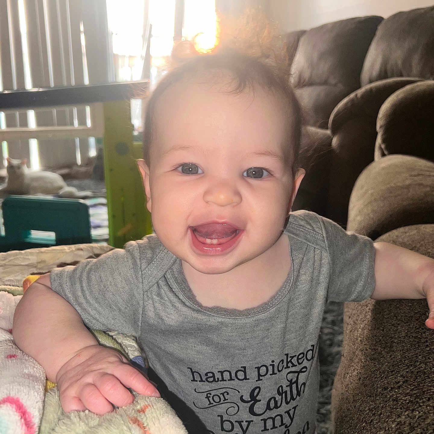 Vidalia is registered to the contest to win money with this photo: arm, baby, blanket, cat, clothing, couch, eyes, face, furniture, hand, happy, indoor, infant, living_room, mouth, person, play_area, smiling, teeth, toy