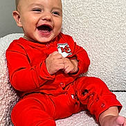 Mylo is registered to the contest to win money with this photo: baby, child, infant, smiling, laughing, red_pajamas, couch, indoor, happy, cute, portrait, sitting, hands, barefoot, cozy, texture, closeup, face, expression, home