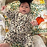 baby, infant, child, portrait, lying_down, smiling, happy, black_bow, headband, leopard_print, outfit, blanket, floral_blanket, autumn_pattern, couch, pillow, indoors, cozy, raised_hand, bare_feet